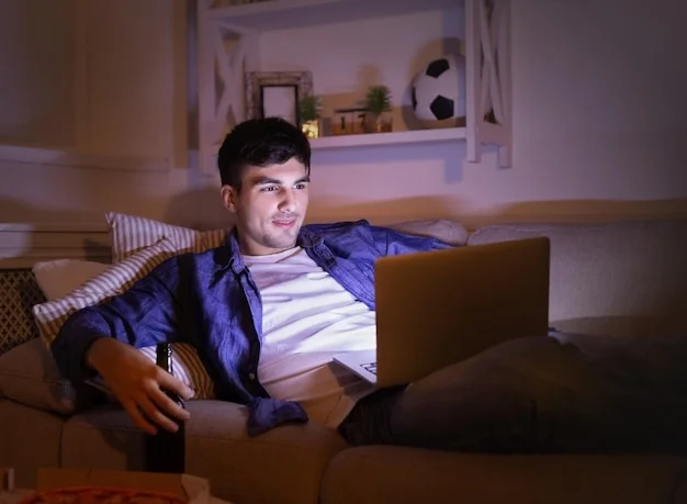 A man sitting on a couch intently watching the screen of a laptop, symbolizing the struggle with porn dependency.