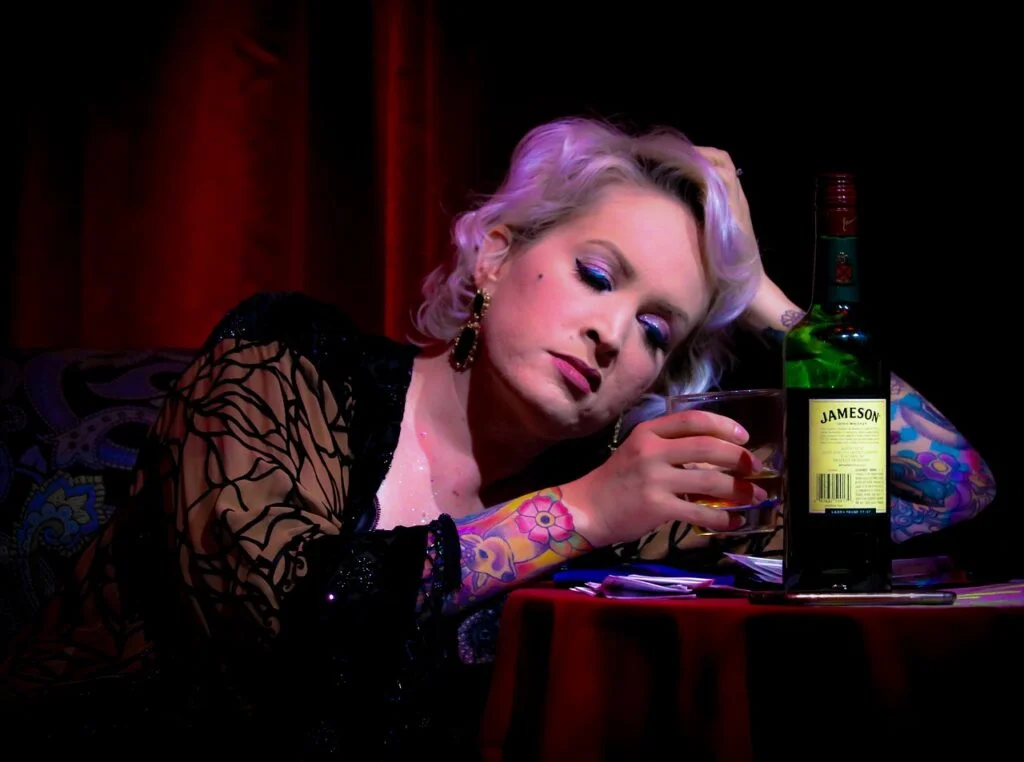 A woman sitting alone and drinking from a glass, illustrating the struggle with alcohol dependency.
