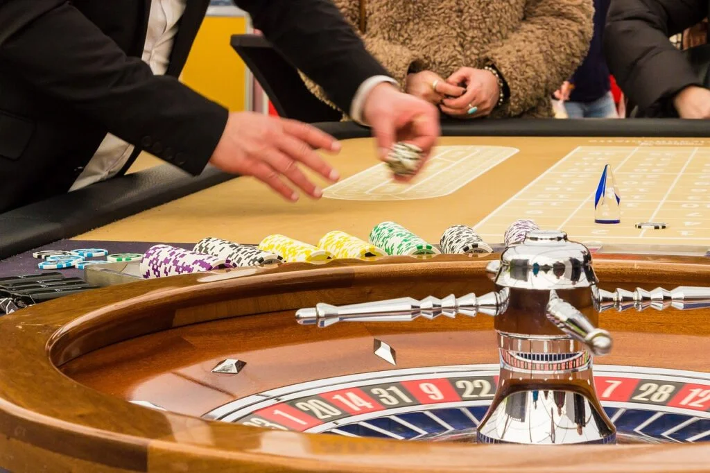 A person sitting at a table holding a stack of poker chips and looking at playing cards, representing the challenge of gambling dependency.