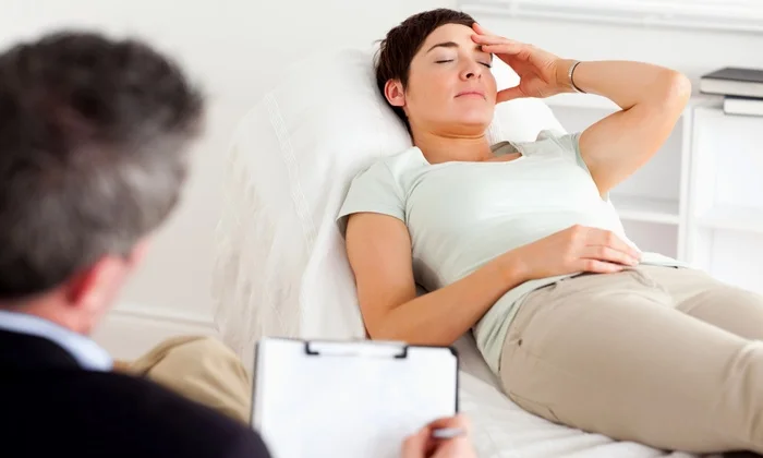 A woman reclining comfortably with her eyes closed while a therapist conducts a hypnotherapy session, illustrating the process of hypnosis.